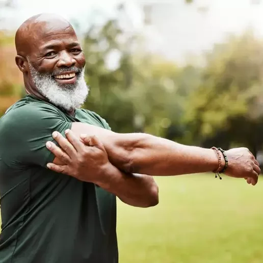 Homem negro com camiseta verde esticando um braço com a ajuda do outro braço. 