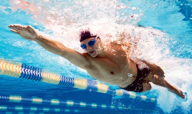 Homem dentro da piscina com óculos de natação nadando