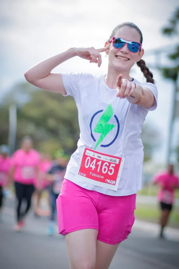 Fabiane, sorrindo e usando camiseta do Hiperativo e shorts rosa durante uma corrida.